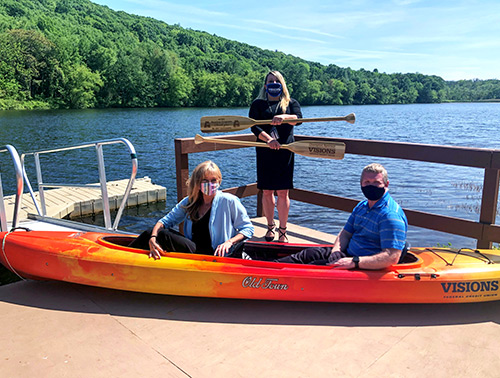 Visions employee Shari Leone sits with Allamuchy School District principal in a docked canoe. The school district's secretary is posing with the oars.
