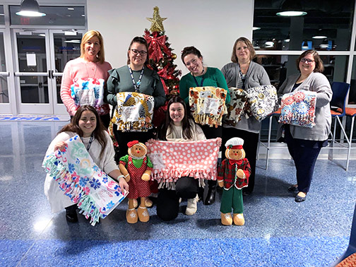 A group of Visions employees pose with their homemade blankets in the cafeteria at Visions Headquarters in Endwell, NY.