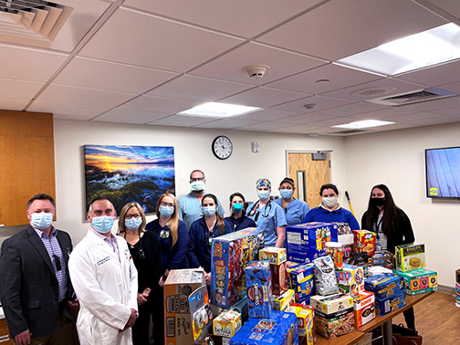 Wearing face coverings, Visions employees Jocelyn and Emily pose with Guthrie Emergency Room staff near a table of donated snacks, drinks, and to-go meals.