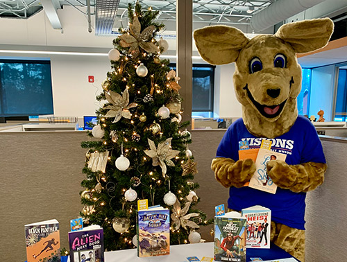 Kirby Kangaroo poses with a table filled with children's books to be donated to Golden Opportunity, and distributed around the Tompkins County area.