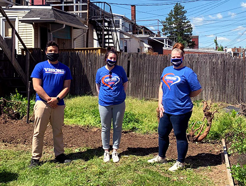 Visions employees Gustavo, Ashley, and Brenna smile for the camera in the garden behind Café Esperanza in Reading, PA.