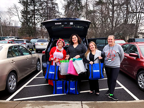 Visions PR Assistant, dressed up as Mrs. Claus, smiles at an open trunk filled with bags of Christmas gifts alongside two Community Development Liaisons and a Northern Broome Cares Rep.