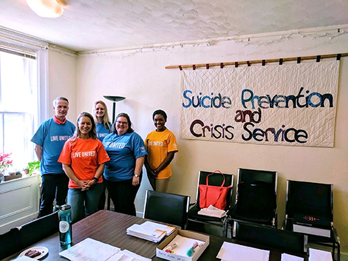 Visions FCU staff wearing “Live United” shirts posing for a group photo next to a sign that reads “Suicide Prevention and Crisis Service”