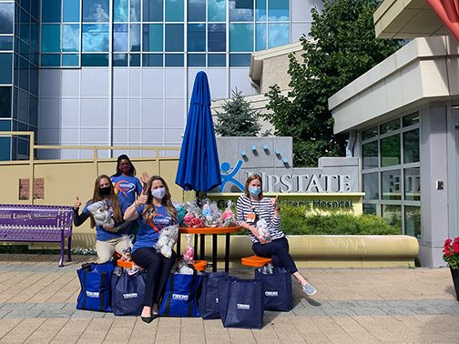 Visions employees Aisha, Emily, and Ashley give a thumbs up as they sit outside Upstate Golisano Children's Hospital to kindly present a nurse with lollipops and stuffed animals for numerous patients as a donation.