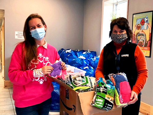 Our Wysox, PA office Branch Manager, Barbara, holds up hats and gloves with a CHOP representative to show some of the winter gear donations our Wysox office employees collected.