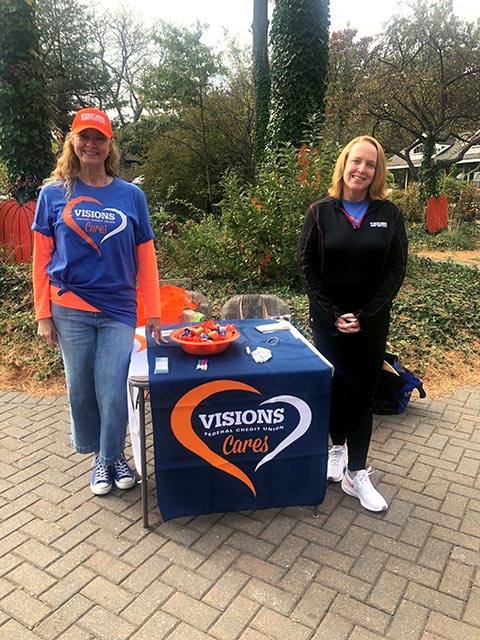 Decked out in Visions apparel, two Visions employees pose at the sponsor table in the Bergen County Zoo, where they gave out free carousel and train rides and Zoo Boo tickets.