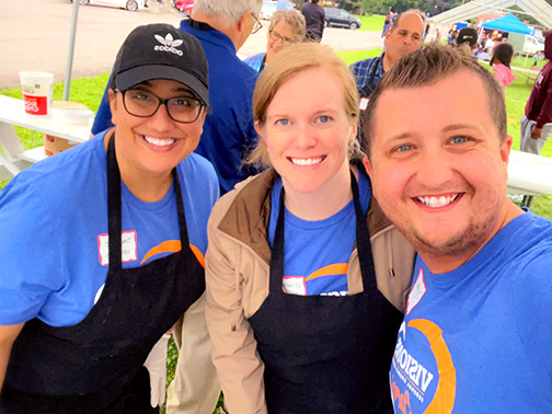Three Visions employees smiling in an outdoor tent getting ready to serve ice cream.