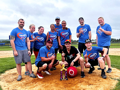 The Visions team posing proudly on a dirt mound with a kickball and trophy.