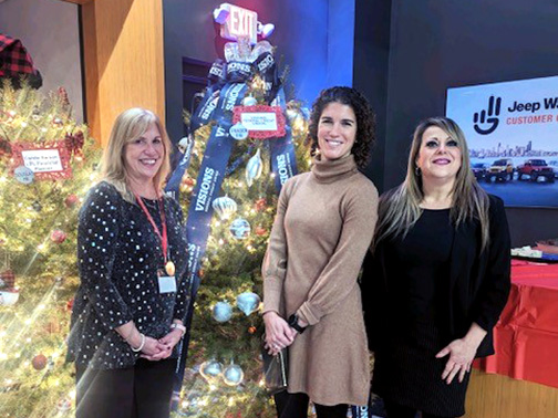 Visions employees Teresa, Jenna, and Kimberly pictured in front of a beautifully decorated Visions Christmas tree.
