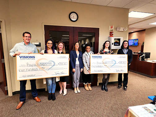 Kenda (Visions FCU), Rayna and Alicia (scholarship winners), Ryan Linn (Interim Director of SUNY Oswego’s Syracuse Campus), and SUNY Oswego staff pictured smiling and holding checks in an office environment.