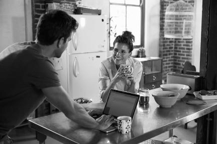 A couple at home working on a laptop drinking coffee