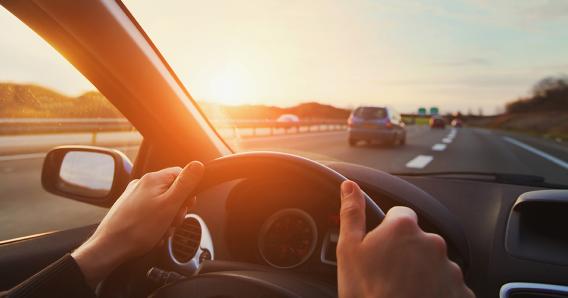 person driving a car with hands on the steering wheel looking out at the road