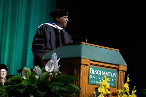 Muse stands at Binghamton University lectern during commencement speach.